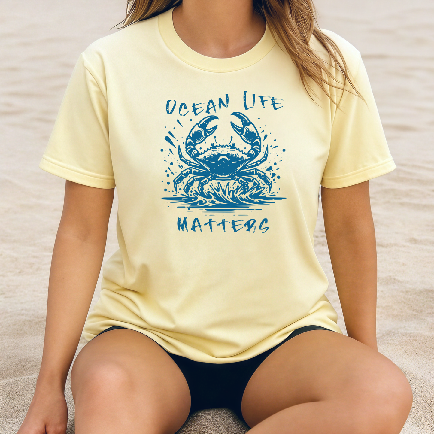 Comfort Colors 1717 "Ocean Life Matters" t shirt with a crab splashing in water in a one color graphic. Picture of a girl sitting on the beach wearing an oversized t shirt.