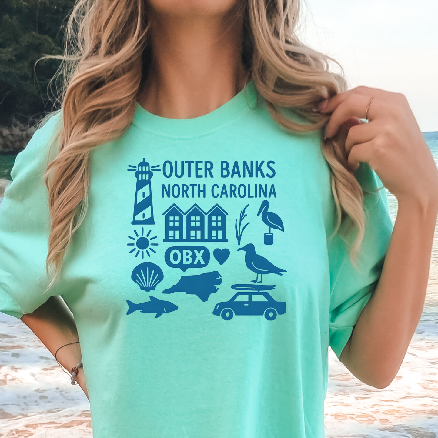 Person wearing a green t-shirt with Outer Banks, North Carolina graphics on a beach.