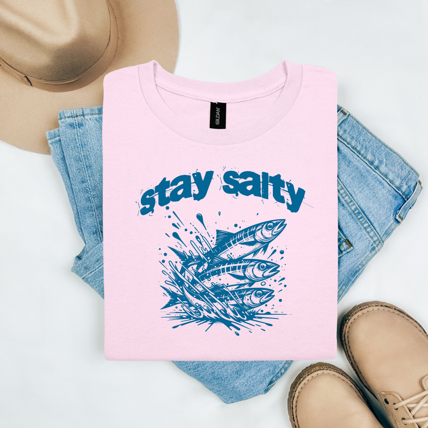 Gildan 5000 "Stay Salty" t shirt with Three Sardines jumping out of water in one color graphics. Picture on a flay lay mockup with pair of blue jeans, brown shoes and a hat accessory.