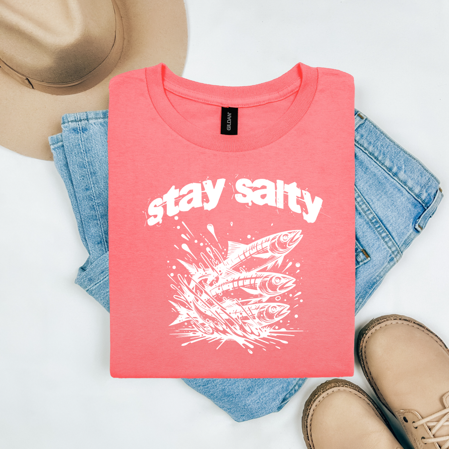 Gildan 5000 "Stay Salty" t shirt with Three Sardines jumping out of water in one color graphics. Picture on a flay lay mockup with pair of blue jeans, brown shoes and a hat accessory.