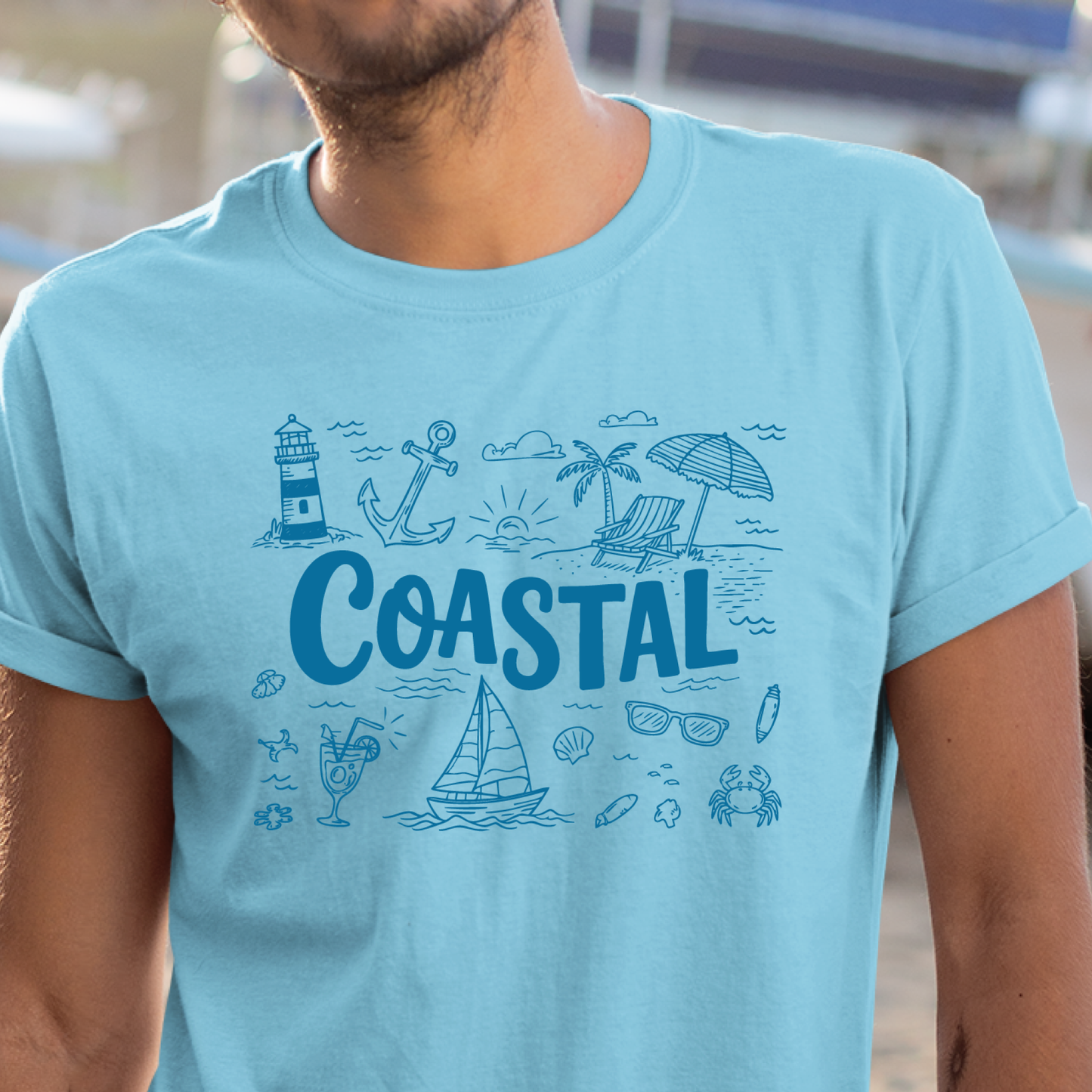 Sky blue t-shirt with coastal design and 'COASTAL' text worn by a person.