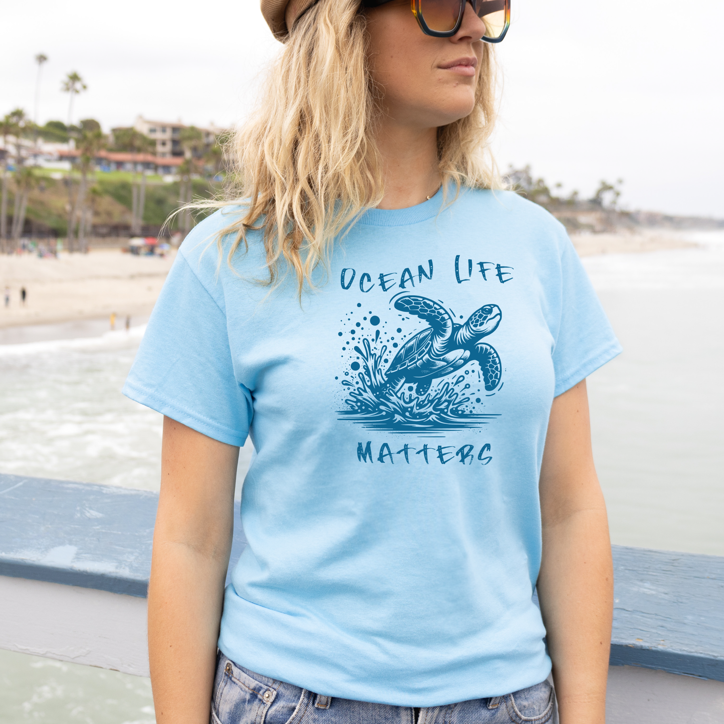 Gildan 5000 "Save The Ocean and The Sea Life In It" t shirt with a sea turtle splashing in water in a one color graphic. Picture of a girl standing on the beach wearing a t shirt.
