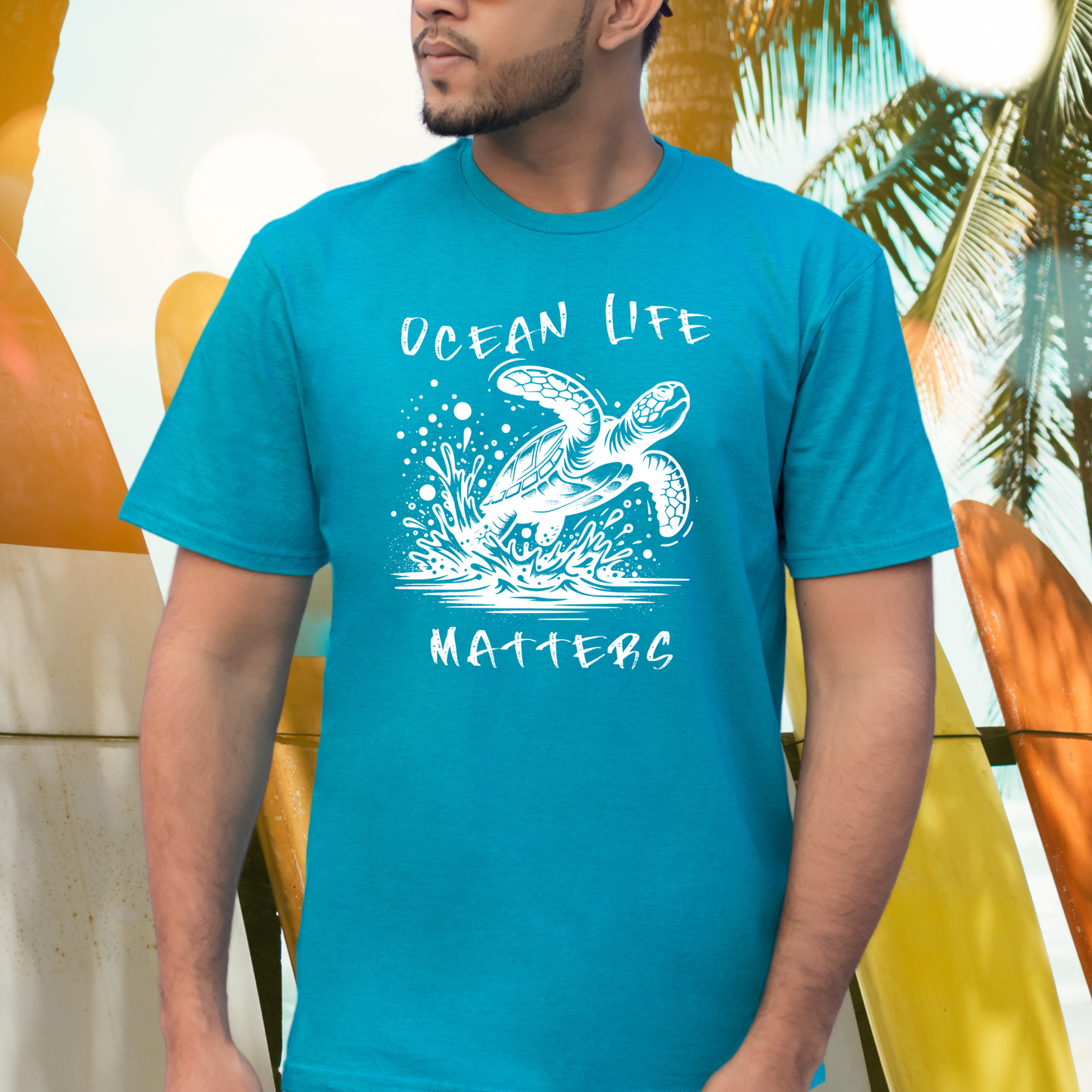 Gildan 5000 "Save The Ocean and The Sea Life In It" t shirt with a sea turtle splashing in water in a one color graphic. Picture of a man standing next to surfboards wearing a t shirt.