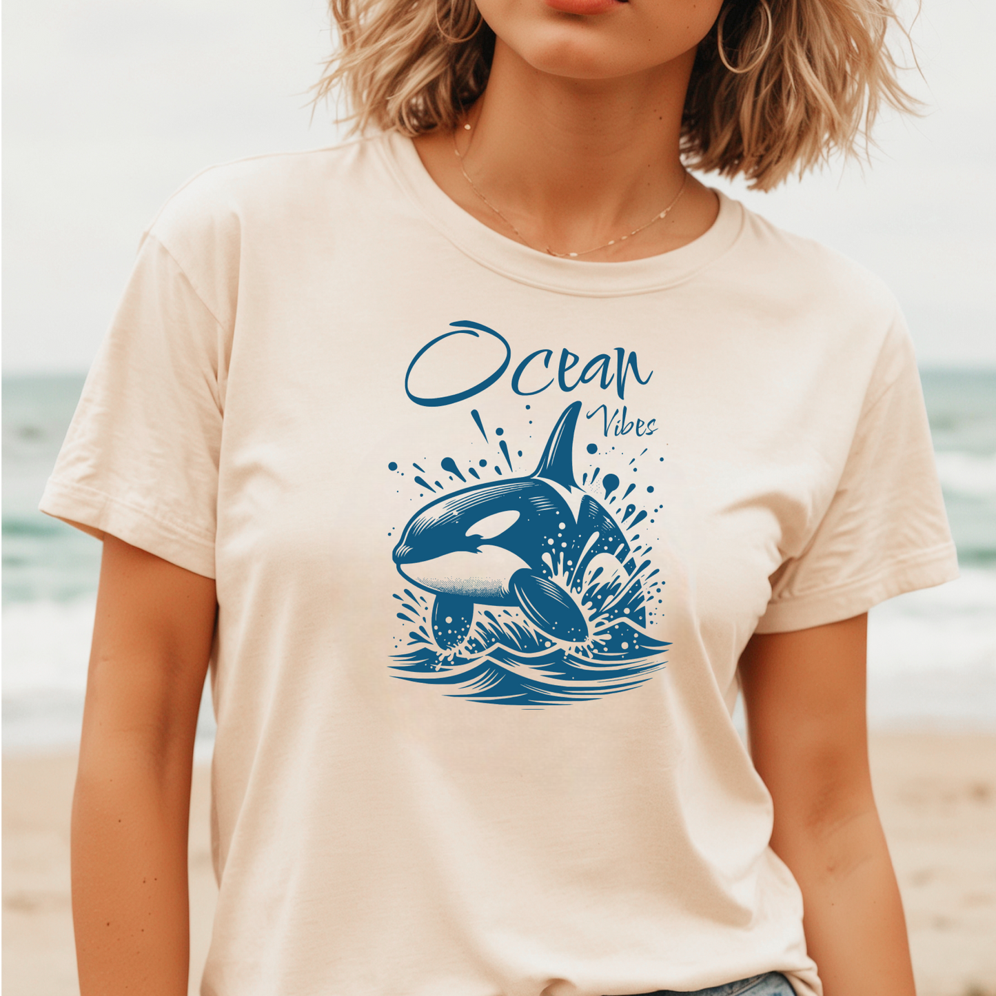Gildan 5000 "Ocean Vibes" t shirt with a orca whale jumping out of water graphics in a one color graphic. Picture of a girl standing on the beach wearing a t shirt.