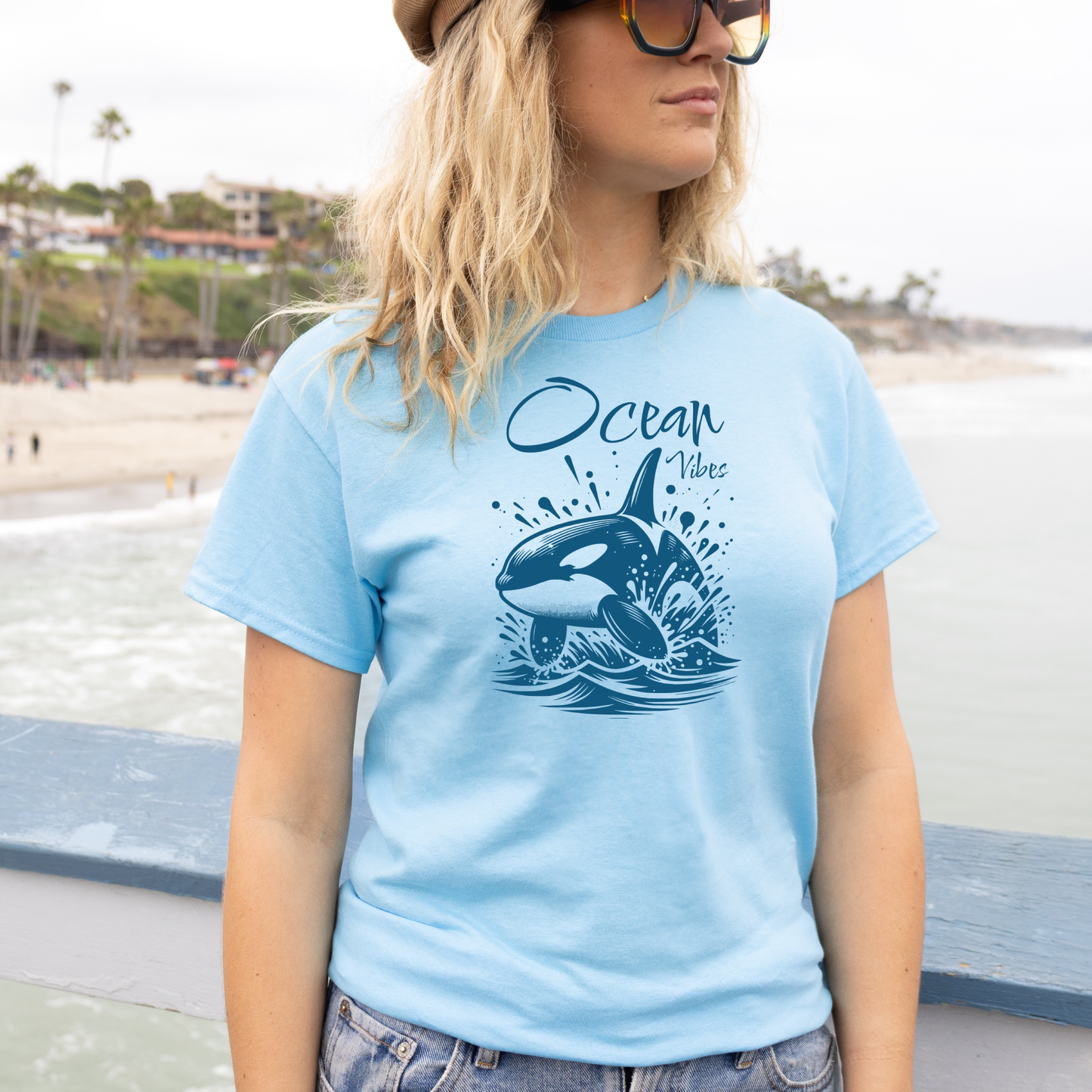 Gildan 5000 "Ocean Vibes" t shirt with a orca whale jumping out of water graphics in a one color graphic. Picture of a girl standing on the beach wearing a t shirt.