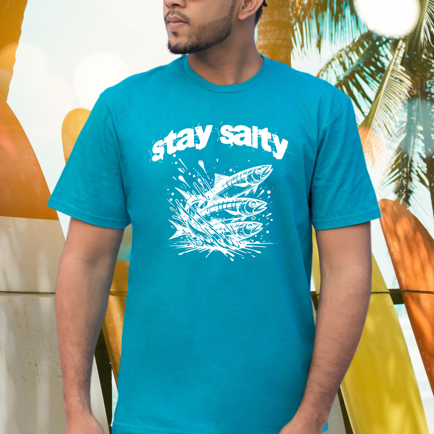 Gildan 5000 "Stay Salty" t shirt with Three Sardines jumping out of water in one color graphics. Picture of a man standing by surfboards wearing a t shirt.