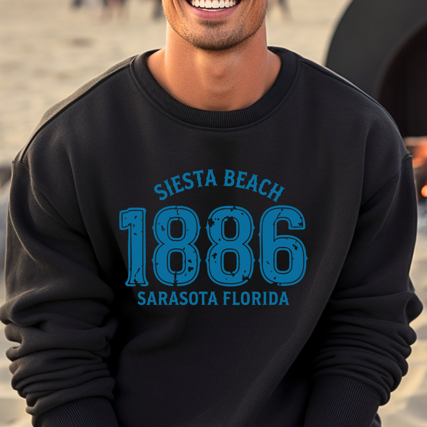 Person wearing a black sweatshirt with blue text 'Siesta Beach 1886 Sarasota Florida' on a beach.