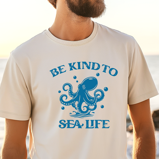 Person wearing a t-shirt with an octopus design and text 'Be Kind to Sea Life' on a beach.
