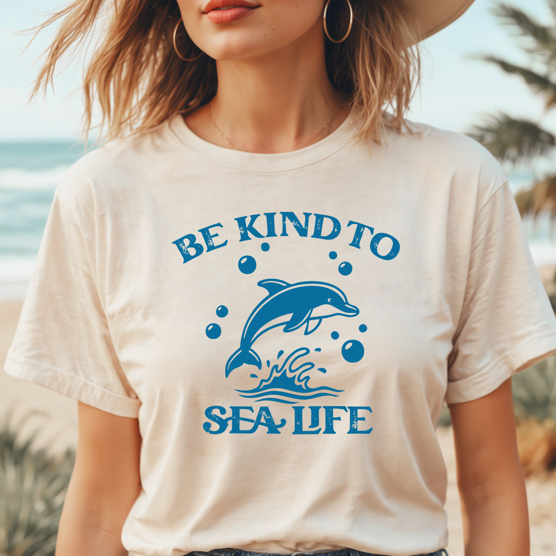 Person wearing a t-shirt with a dolphin graphic and 'Be Kind to Sea Life' text on a beach.