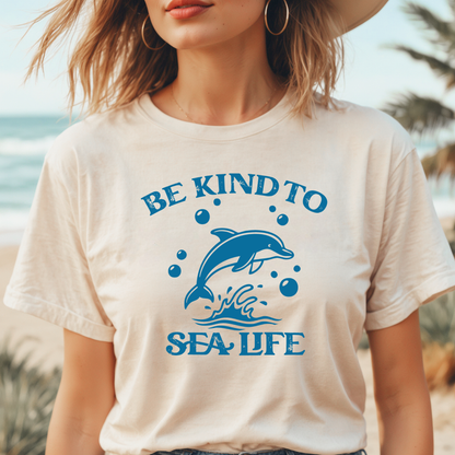 Person wearing a t-shirt with a dolphin graphic and 'Be Kind to Sea Life' text on a beach.