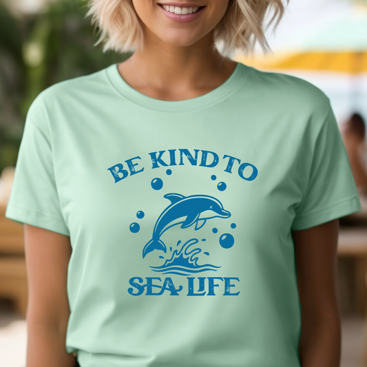 Person wearing a light green t-shirt with a dolphin graphic and 'Be Kind to Sea Life' text.