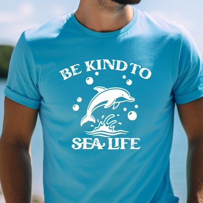 Person wearing a aqua blue t-shirt with a dolphin graphic and text 'Be Kind to Sea Life'.