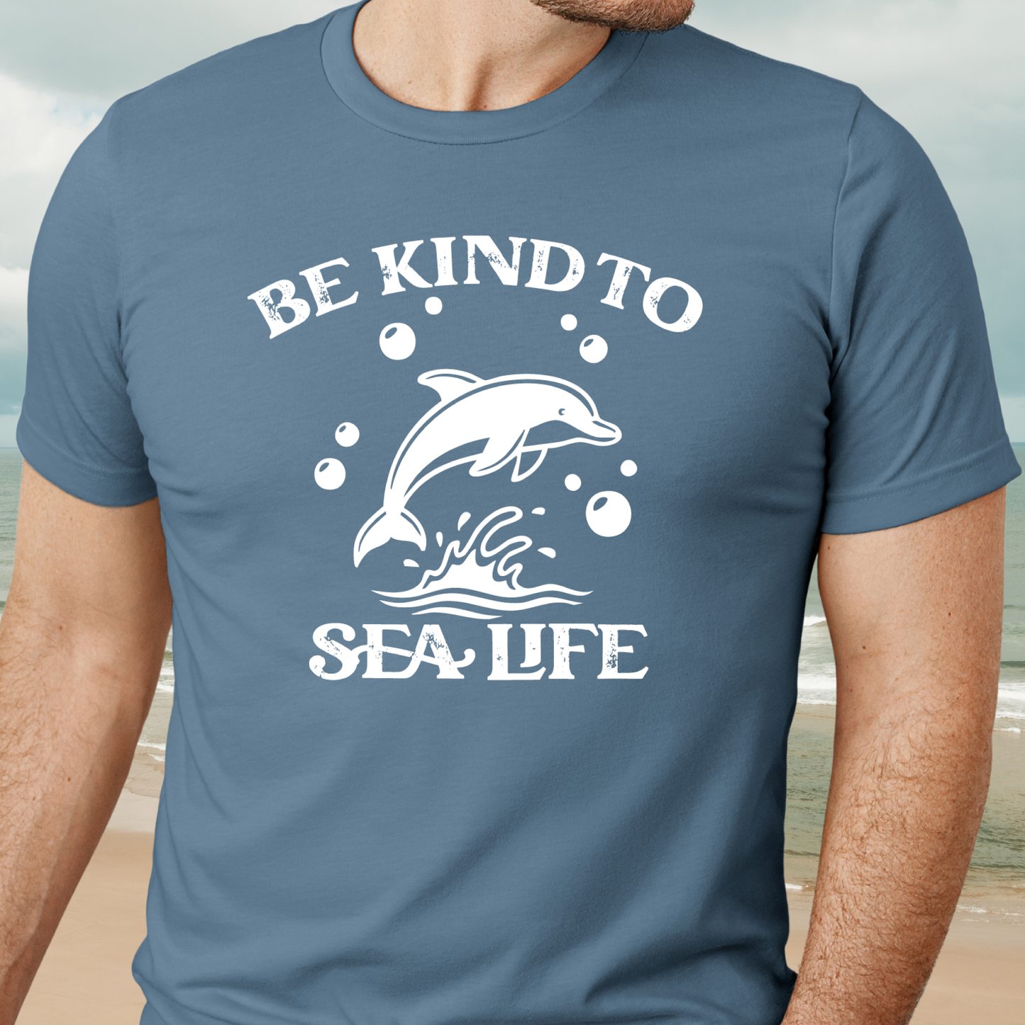 Steel Blue t-shirt with a dolphin graphic and 'Be Kind to Sea Life' text on a beach background
