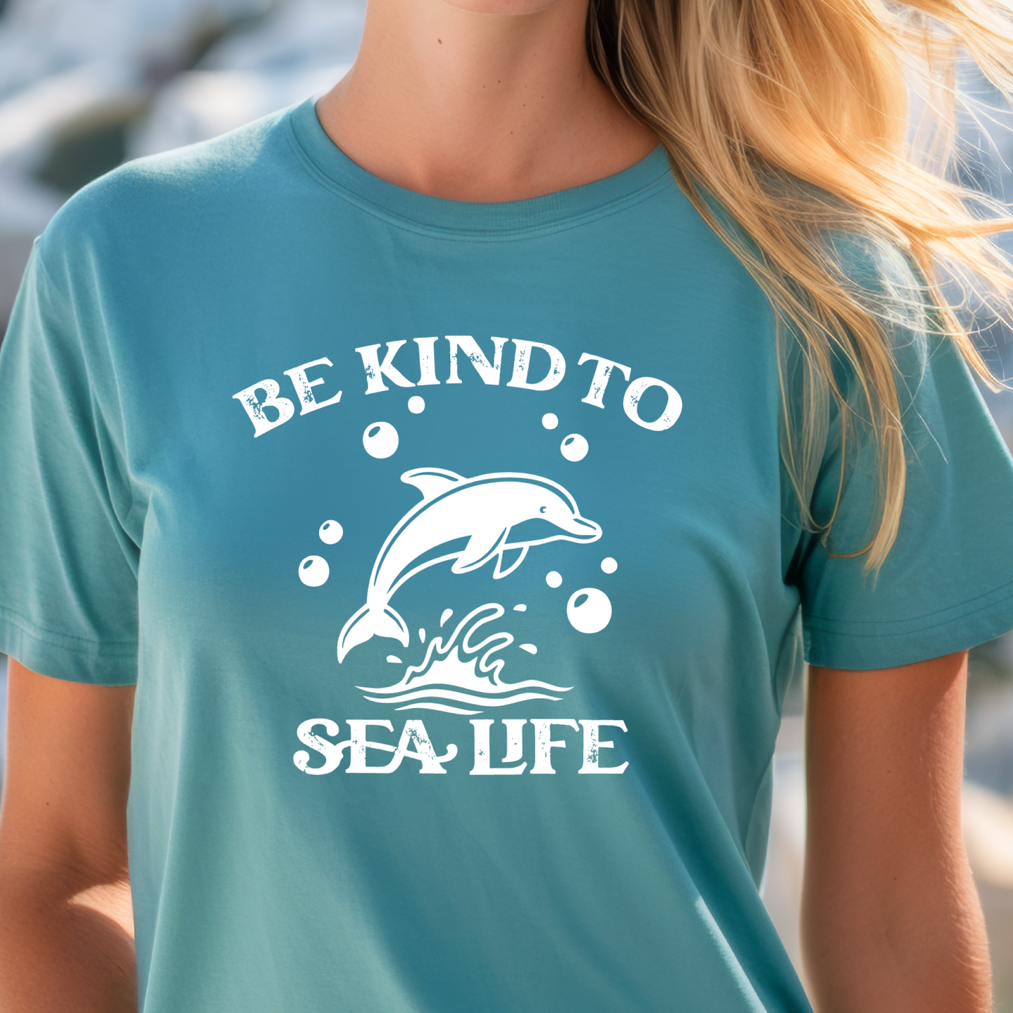 Person wearing a turquoise t-shirt with a dolphin graphic and 'Be Kind to Sea Life' text.