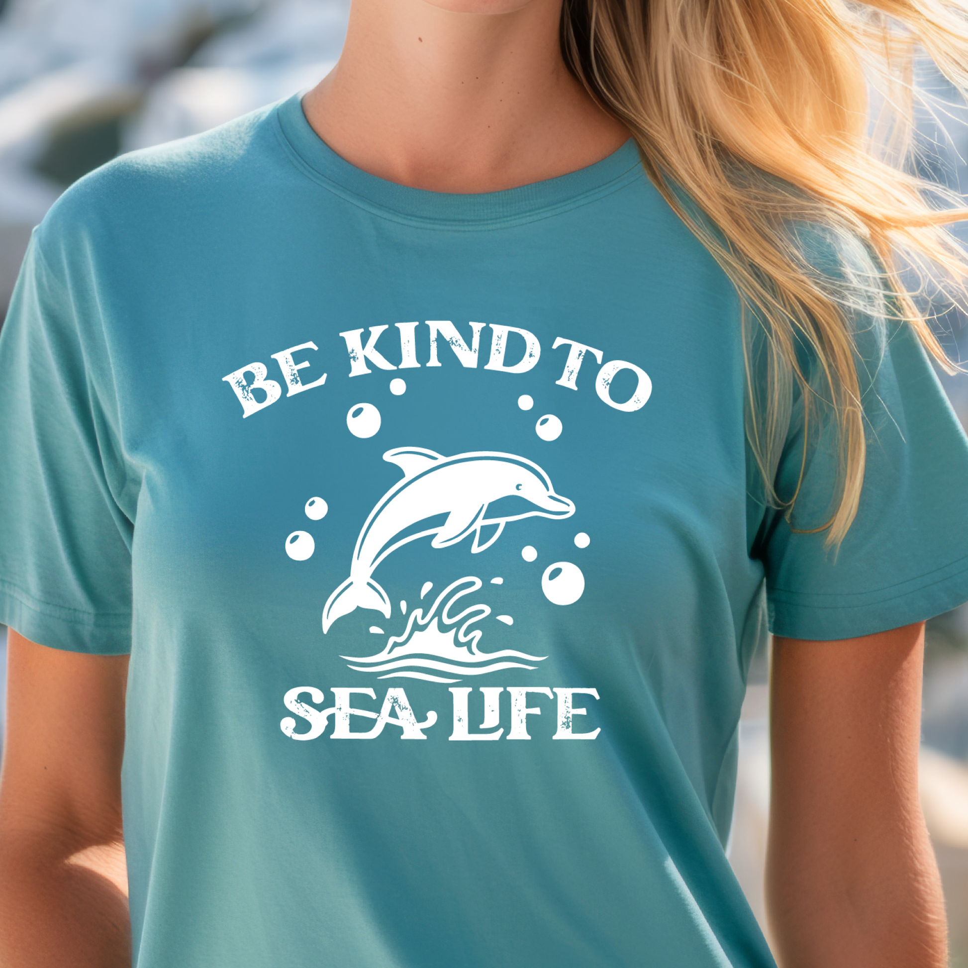 Person wearing a turquoise t-shirt with a dolphin graphic and 'Be Kind to Sea Life' text.