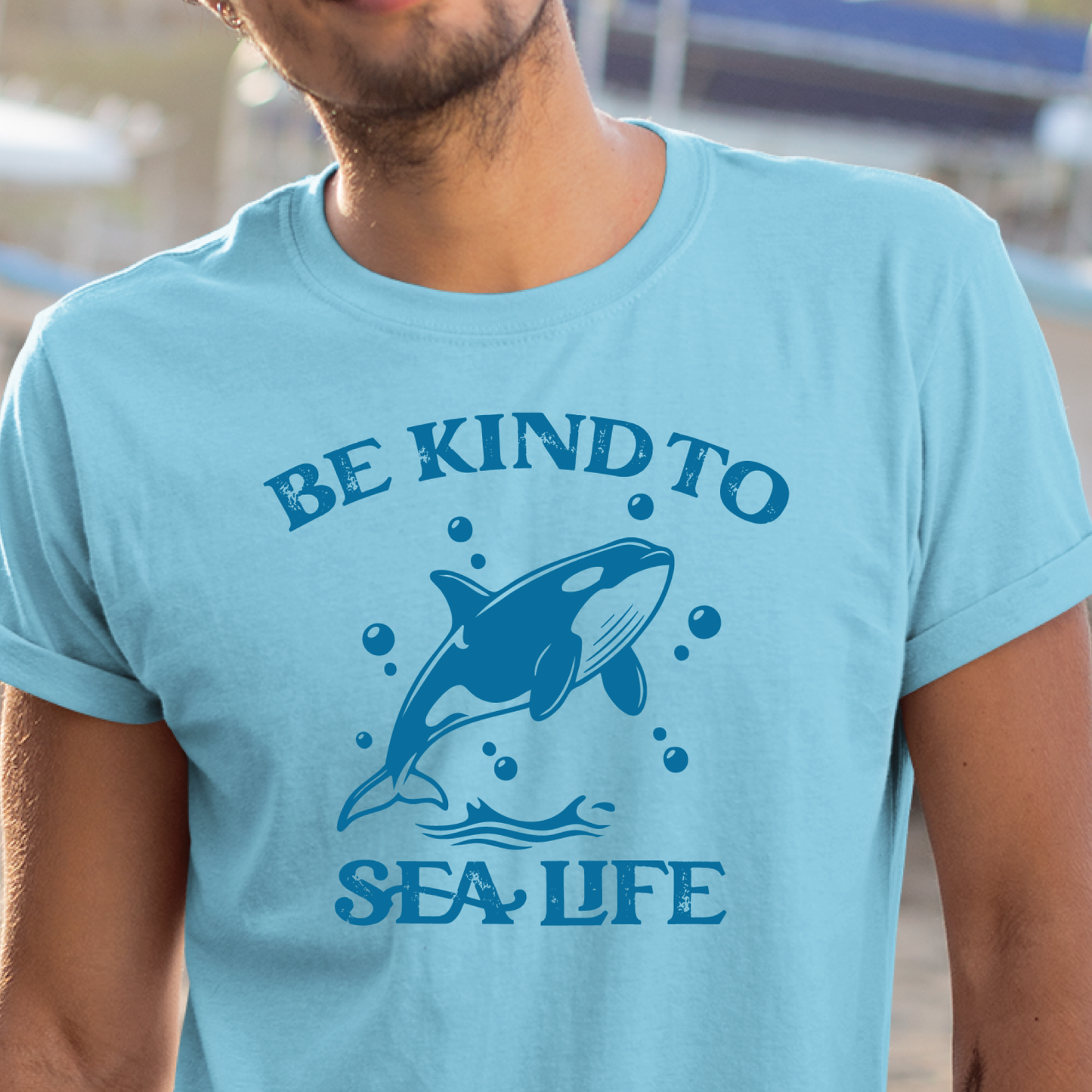 Person wearing a light blue t-shirt with a whale graphic and text 'Be Kind to Sea Life'.