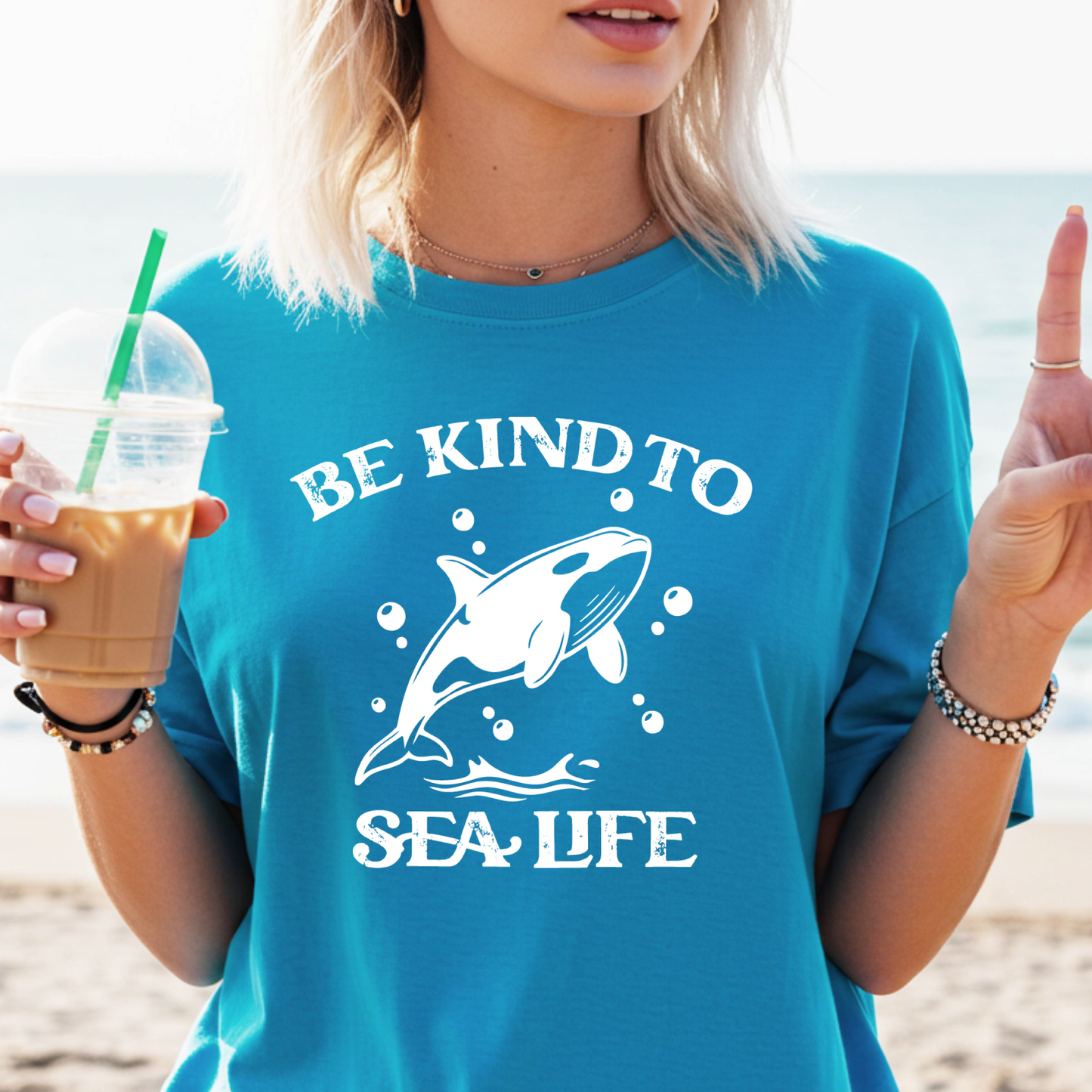 Person wearing a sapphire blue t-shirt with a whale graphic and 'Be Kind to Sea Life' text on a beach.