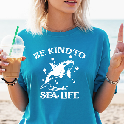 Person wearing a sapphire blue t-shirt with a whale graphic and 'Be Kind to Sea Life' text on a beach.