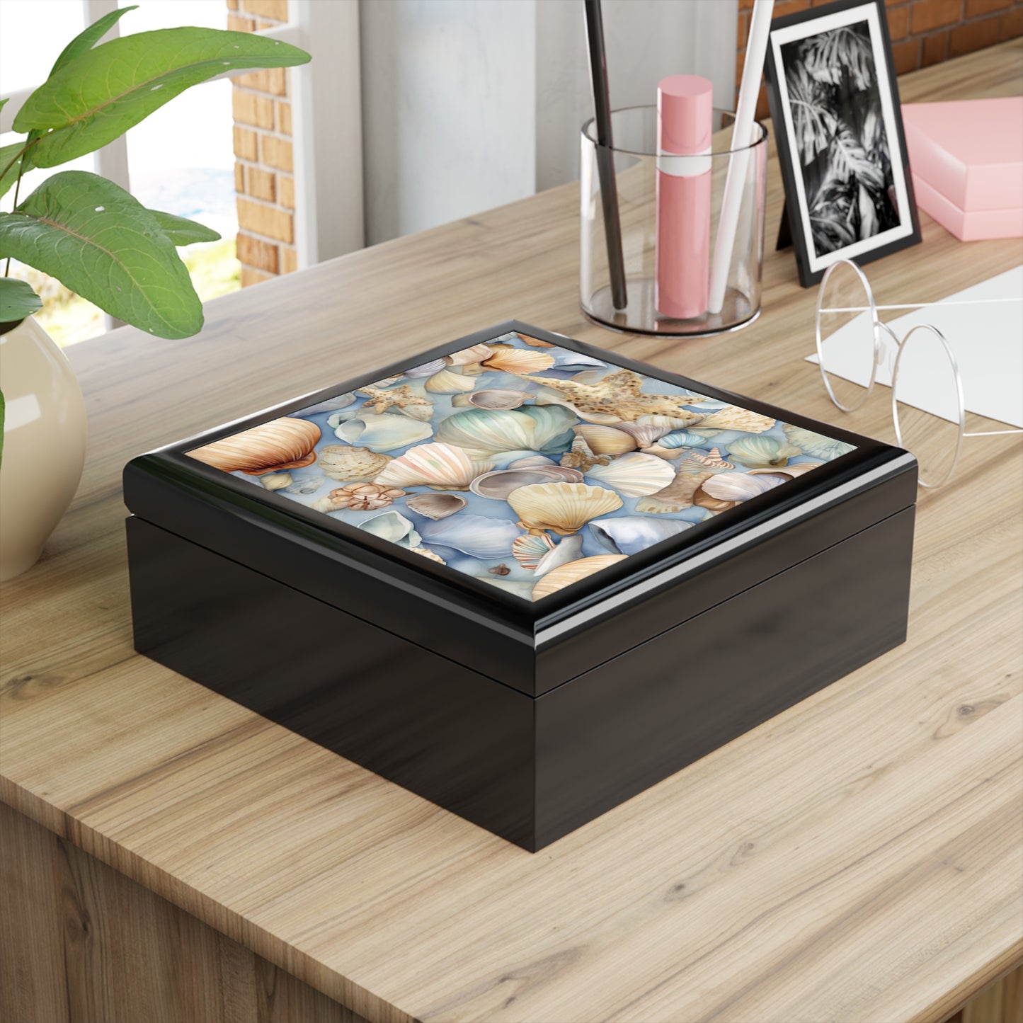 A Coastal Shells Jewelry Box - Nautical Beach Decor for Organizing Treasures rests on the wooden table. Nearby are glasses, a pencil holder with pens, and a small plant, enhancing the nautical-themed decor. A framed photo is partially visible in the background.