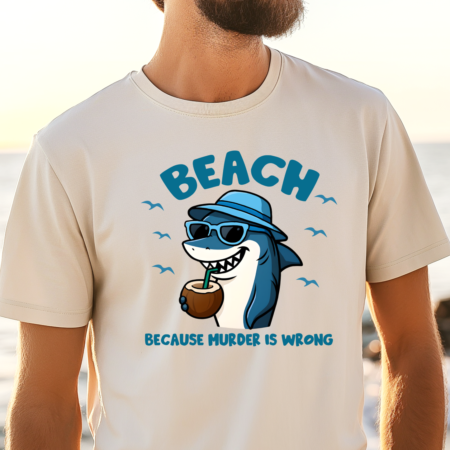 Person wearing a t-shirt with a shark graphic and text at the beach