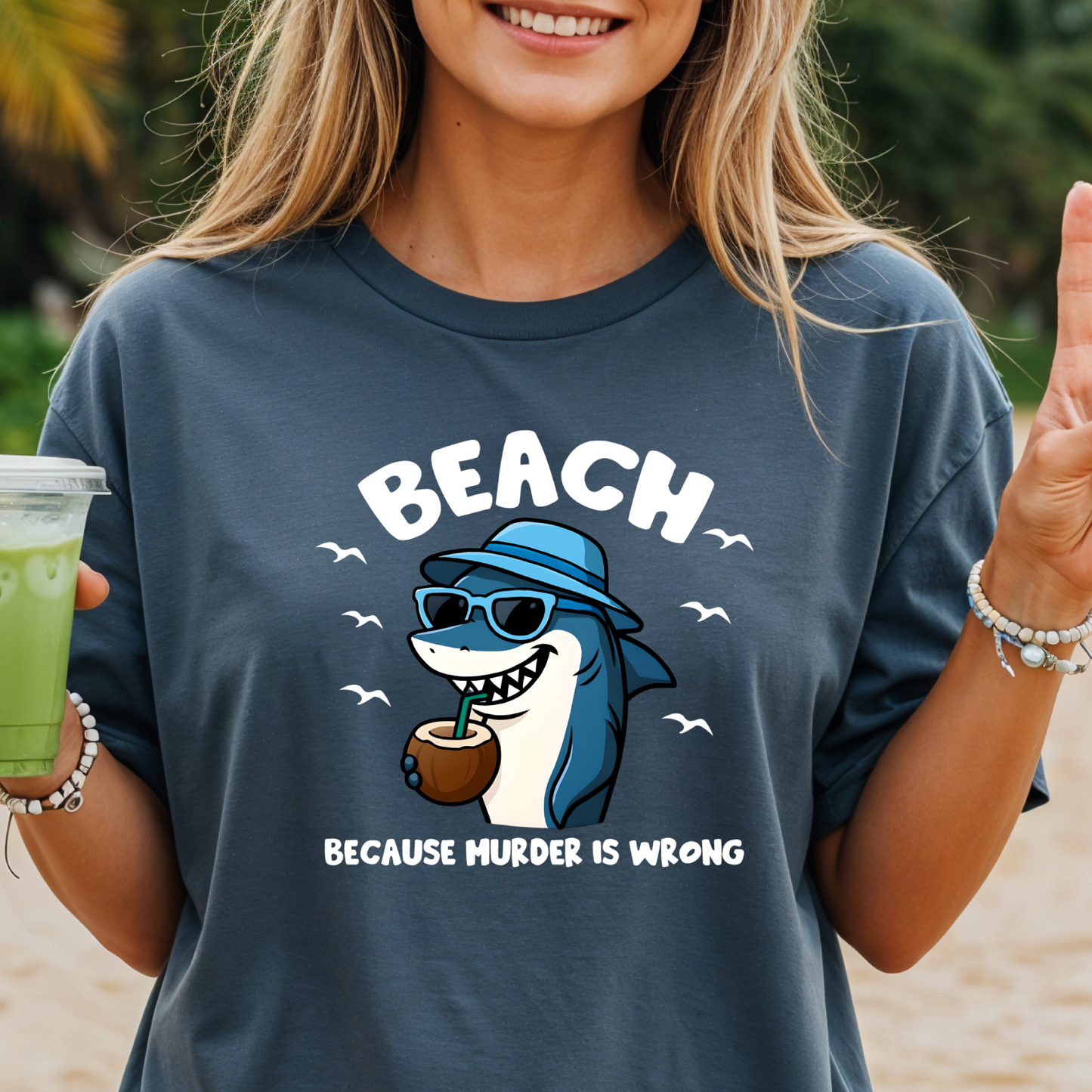 Person wearing a t-shirt with a shark graphic and text on a beach.