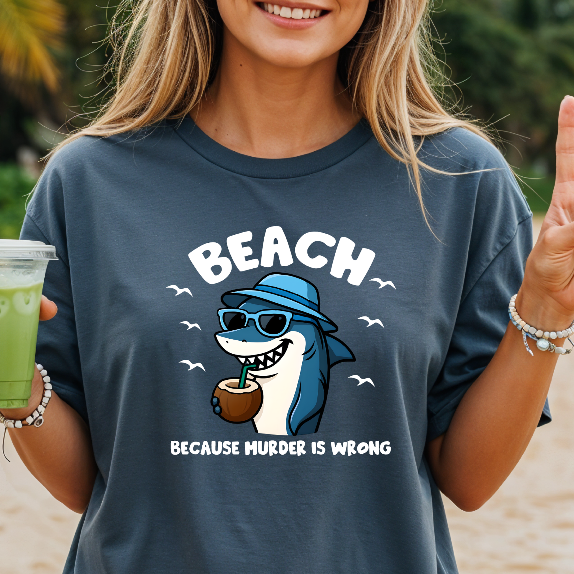Person wearing a t-shirt with a shark graphic and text on a beach.