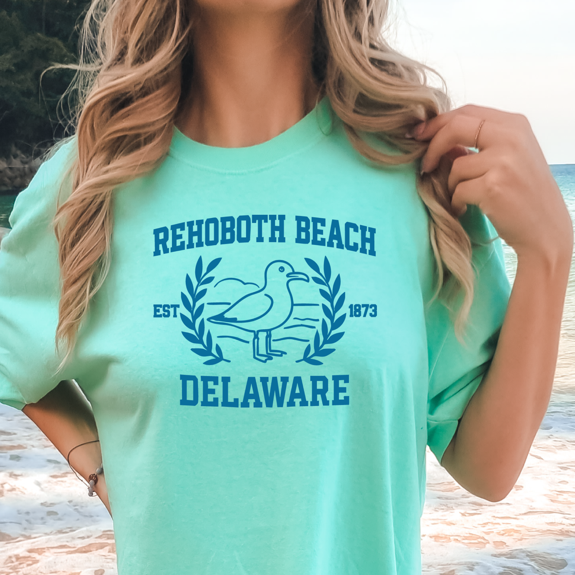 Person wearing a island reef t-shirt with Rehoboth Beach, Delaware text and logo on a beach.