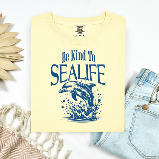 A Comfort Colors t-shirt with a soft, broken-in feel and a relaxed, vintage look. The front features a simple graphic of a dolphin gracefully jumping out of the ocean, drawn in clean lines with a calm, coastal vibe.