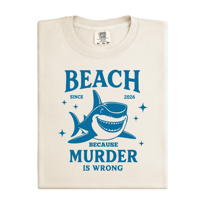 Comfort Colors t-shirt featuring a blue cartoon shark illustration with the humorous text “Beach Because Murder Is Wrong” and “Since 2026.” The design includes sparkling star accents for a fun coastal look. This unisex garment-dyed tee offers soft, vintage-style cotton and a relaxed fit, perfect for beach lovers, humor fans, and anyone who enjoys playful ocean-themed graphic shirts.