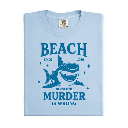 Comfort Colors t-shirt featuring a blue cartoon shark illustration with the humorous text “Beach Because Murder Is Wrong” and “Since 2026.” The design includes sparkling star accents for a fun coastal look. This unisex garment-dyed tee offers soft, vintage-style cotton and a relaxed fit, perfect for beach lovers, humor fans, and anyone who enjoys playful ocean-themed graphic shirts.