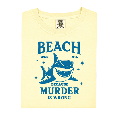 Comfort Colors t-shirt featuring a blue cartoon shark illustration with the humorous text “Beach Because Murder Is Wrong” and “Since 2026.” The design includes sparkling star accents for a fun coastal look. This unisex garment-dyed tee offers soft, vintage-style cotton and a relaxed fit, perfect for beach lovers, humor fans, and anyone who enjoys playful ocean-themed graphic shirts.