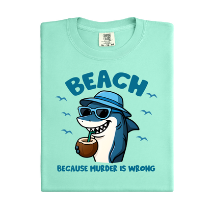 Light green t-shirt with a cartoon shark wearing sunglasses and a hat, holding a coconut, and text 'BEACH BECAUSE MURDER IS WRONG' on a white background.