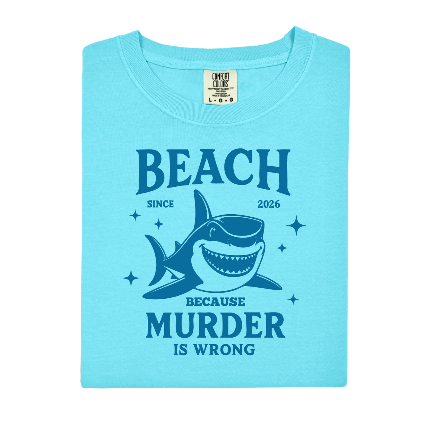 Comfort Colors t-shirt featuring a blue cartoon shark illustration with the humorous text “Beach Because Murder Is Wrong” and “Since 2026.” The design includes sparkling star accents for a fun coastal look. This unisex garment-dyed tee offers soft, vintage-style cotton and a relaxed fit, perfect for beach lovers, humor fans, and anyone who enjoys playful ocean-themed graphic shirts.