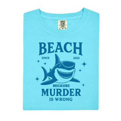 Comfort Colors t-shirt featuring a blue cartoon shark illustration with the humorous text “Beach Because Murder Is Wrong” and “Since 2026.” The design includes sparkling star accents for a fun coastal look. This unisex garment-dyed tee offers soft, vintage-style cotton and a relaxed fit, perfect for beach lovers, humor fans, and anyone who enjoys playful ocean-themed graphic shirts.