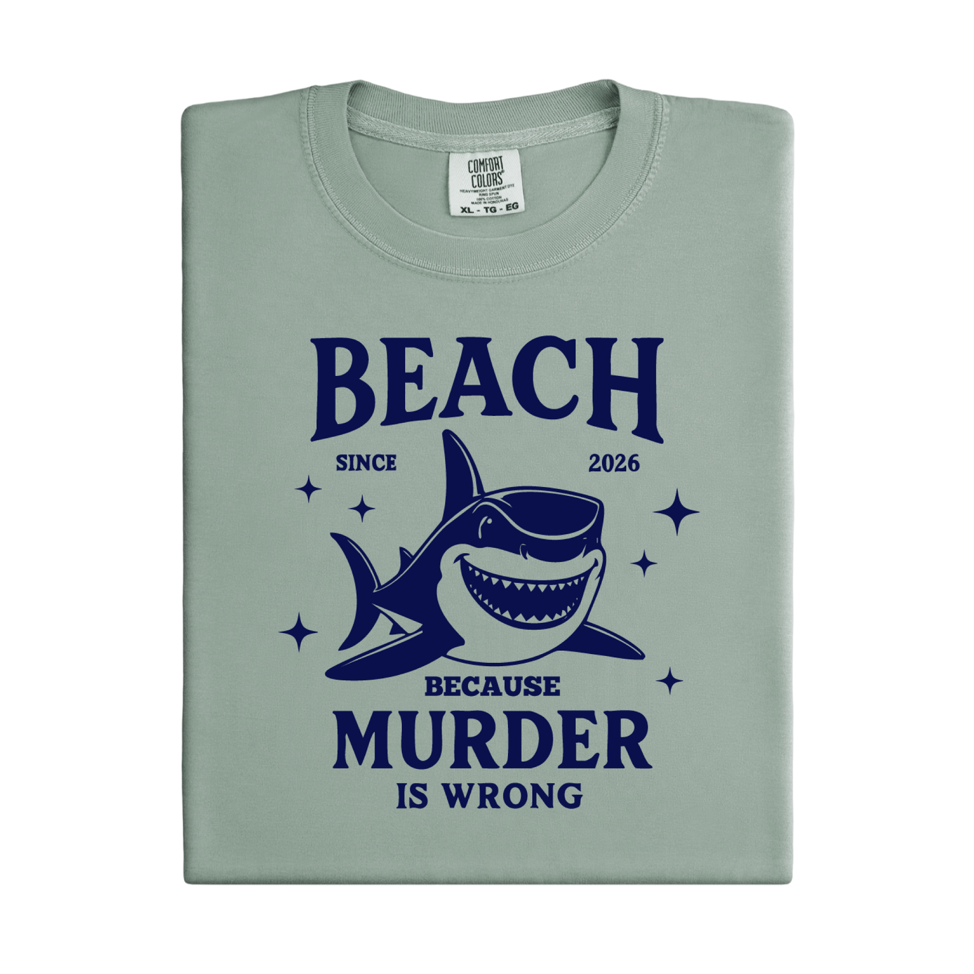 Comfort Colors t-shirt featuring a blue cartoon shark illustration with the humorous text “Beach Because Murder Is Wrong” and “Since 2026.” The design includes sparkling star accents for a fun coastal look. This unisex garment-dyed tee offers soft, vintage-style cotton and a relaxed fit, perfect for beach lovers, humor fans, and anyone who enjoys playful ocean-themed graphic shirts.