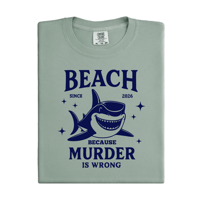 Comfort Colors t-shirt featuring a blue cartoon shark illustration with the humorous text “Beach Because Murder Is Wrong” and “Since 2026.” The design includes sparkling star accents for a fun coastal look. This unisex garment-dyed tee offers soft, vintage-style cotton and a relaxed fit, perfect for beach lovers, humor fans, and anyone who enjoys playful ocean-themed graphic shirts.