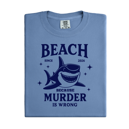 Comfort Colors t-shirt featuring a blue cartoon shark illustration with the humorous text “Beach Because Murder Is Wrong” and “Since 2026.” The design includes sparkling star accents for a fun coastal look. This unisex garment-dyed tee offers soft, vintage-style cotton and a relaxed fit, perfect for beach lovers, humor fans, and anyone who enjoys playful ocean-themed graphic shirts.