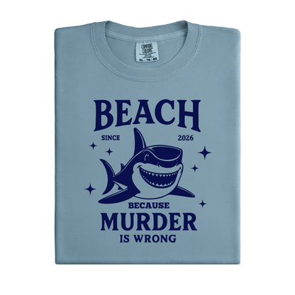 Comfort Colors t-shirt featuring a blue cartoon shark illustration with the humorous text “Beach Because Murder Is Wrong” and “Since 2026.” The design includes sparkling star accents for a fun coastal look. This unisex garment-dyed tee offers soft, vintage-style cotton and a relaxed fit, perfect for beach lovers, humor fans, and anyone who enjoys playful ocean-themed graphic shirts.