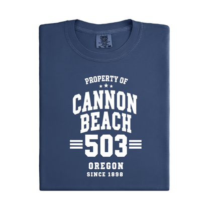 Folded navy blue t-shirt with white text 'Property of Cannon Beach 503 Oregon Since 1898' on a white background