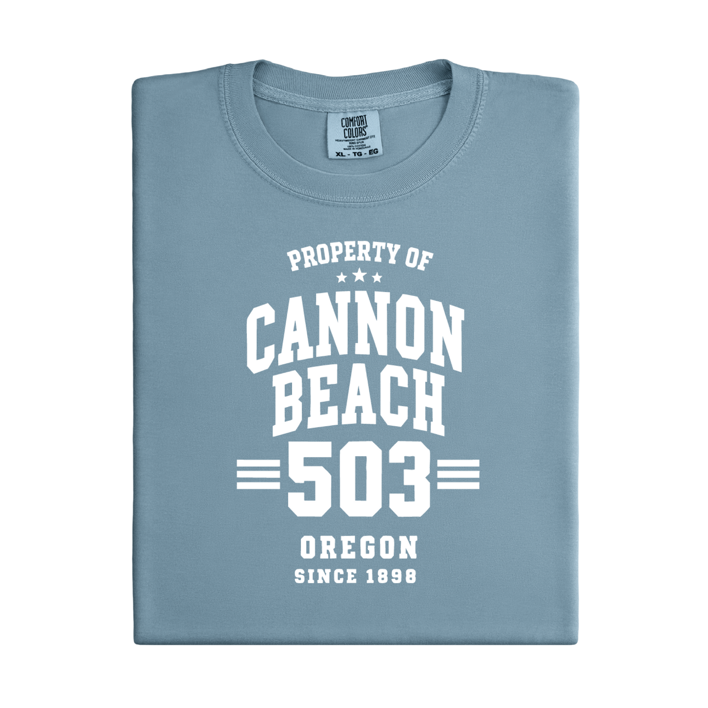 Folded blue t-shirt with white text 'Property of Cannon Beach 503 Oregon Since 1899' on a white background