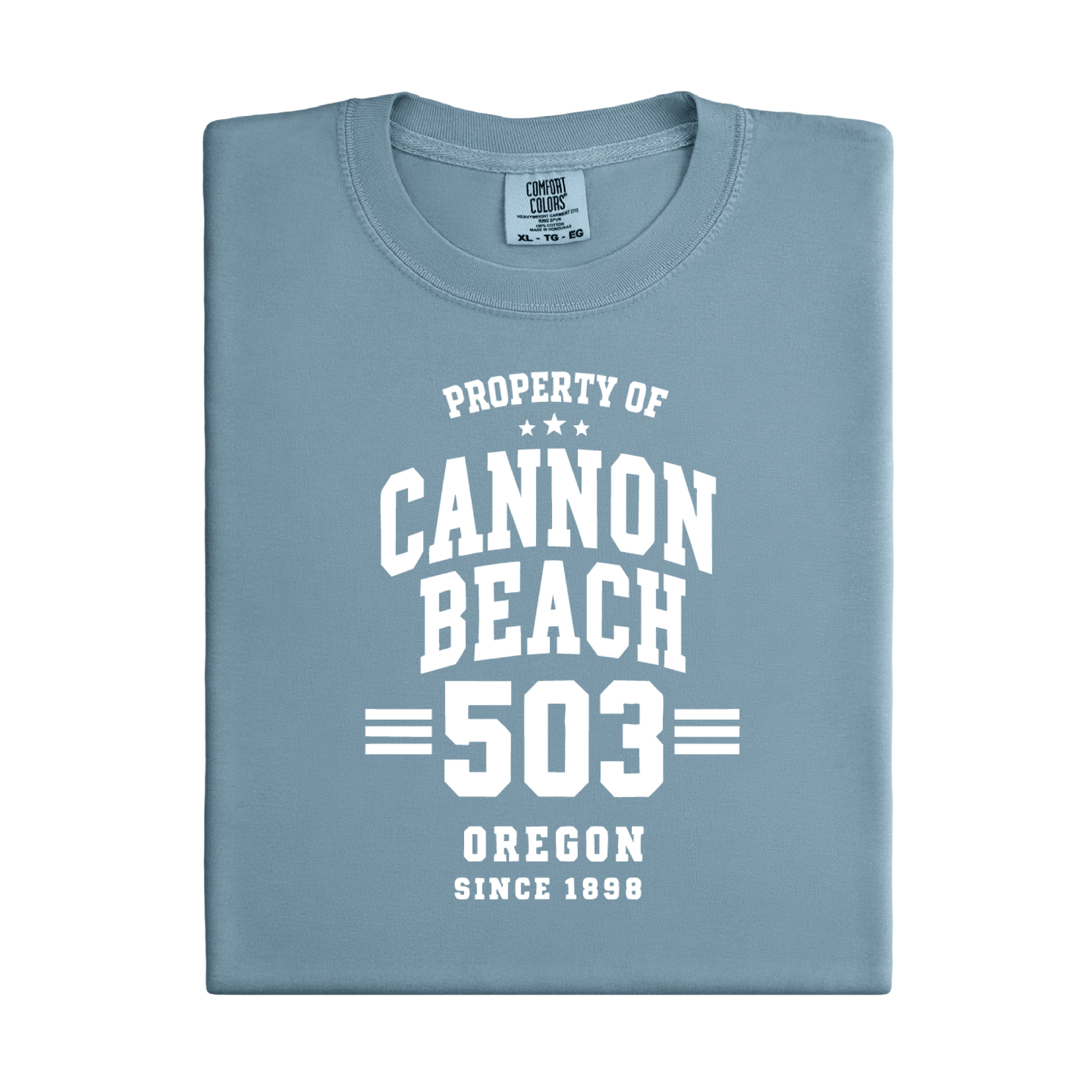 Folded blue t-shirt with white text 'Property of Cannon Beach 503 Oregon Since 1899' on a white background