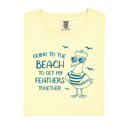 Comfort Colors t-shirt featuring a humorous blue seagull graphic wearing sunglasses and a striped shirt, beside the text “Going to the Beach to Get My Feathers Together.” Several flying birds surround the design, adding a fun coastal feel. This unisex garment-dyed tee offers a soft, vintage texture and relaxed fit, perfect for beach lovers, ocean fans, and anyone who enjoys playful summer graphic shirts.