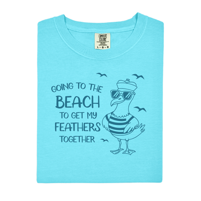 Comfort Colors t-shirt featuring a humorous blue seagull graphic wearing sunglasses and a striped shirt, beside the text “Going to the Beach to Get My Feathers Together.” Several flying birds surround the design, adding a fun coastal feel. This unisex garment-dyed tee offers a soft, vintage texture and relaxed fit, perfect for beach lovers, ocean fans, and anyone who enjoys playful summer graphic shirts.