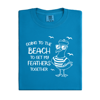 Comfort Colors t-shirt featuring a humorous blue seagull graphic wearing sunglasses and a striped shirt, beside the text “Going to the Beach to Get My Feathers Together.” Several flying birds surround the design, adding a fun coastal feel. This unisex garment-dyed tee offers a soft, vintage texture and relaxed fit, perfect for beach lovers, ocean fans, and anyone who enjoys playful summer graphic shirts.