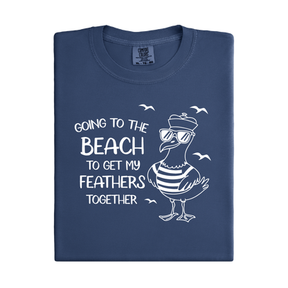 Comfort Colors t-shirt featuring a humorous blue seagull graphic wearing sunglasses and a striped shirt, beside the text “Going to the Beach to Get My Feathers Together.” Several flying birds surround the design, adding a fun coastal feel. This unisex garment-dyed tee offers a soft, vintage texture and relaxed fit, perfect for beach lovers, ocean fans, and anyone who enjoys playful summer graphic shirts.