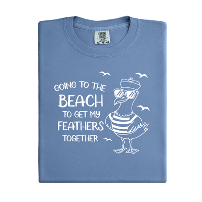 Comfort Colors t-shirt featuring a humorous blue seagull graphic wearing sunglasses and a striped shirt, beside the text “Going to the Beach to Get My Feathers Together.” Several flying birds surround the design, adding a fun coastal feel. This unisex garment-dyed tee offers a soft, vintage texture and relaxed fit, perfect for beach lovers, ocean fans, and anyone who enjoys playful summer graphic shirts.