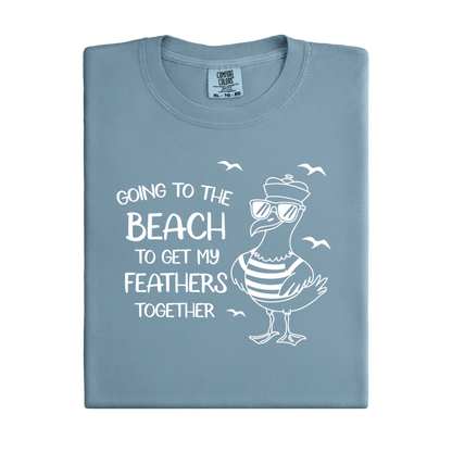 Comfort Colors t-shirt featuring a humorous blue seagull graphic wearing sunglasses and a striped shirt, beside the text “Going to the Beach to Get My Feathers Together.” Several flying birds surround the design, adding a fun coastal feel. This unisex garment-dyed tee offers a soft, vintage texture and relaxed fit, perfect for beach lovers, ocean fans, and anyone who enjoys playful summer graphic shirts.