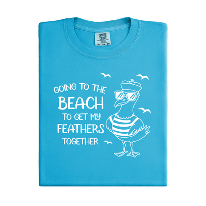 Comfort Colors t-shirt featuring a humorous blue seagull graphic wearing sunglasses and a striped shirt, beside the text “Going to the Beach to Get My Feathers Together.” Several flying birds surround the design, adding a fun coastal feel. This unisex garment-dyed tee offers a soft, vintage texture and relaxed fit, perfect for beach lovers, ocean fans, and anyone who enjoys playful summer graphic shirts.