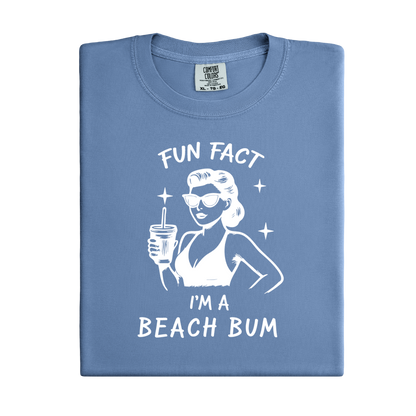 Folded blue t-shirt with a graphic of a woman at the beach and text 'Fun Fact I'm a Beach Bum' on a white background.