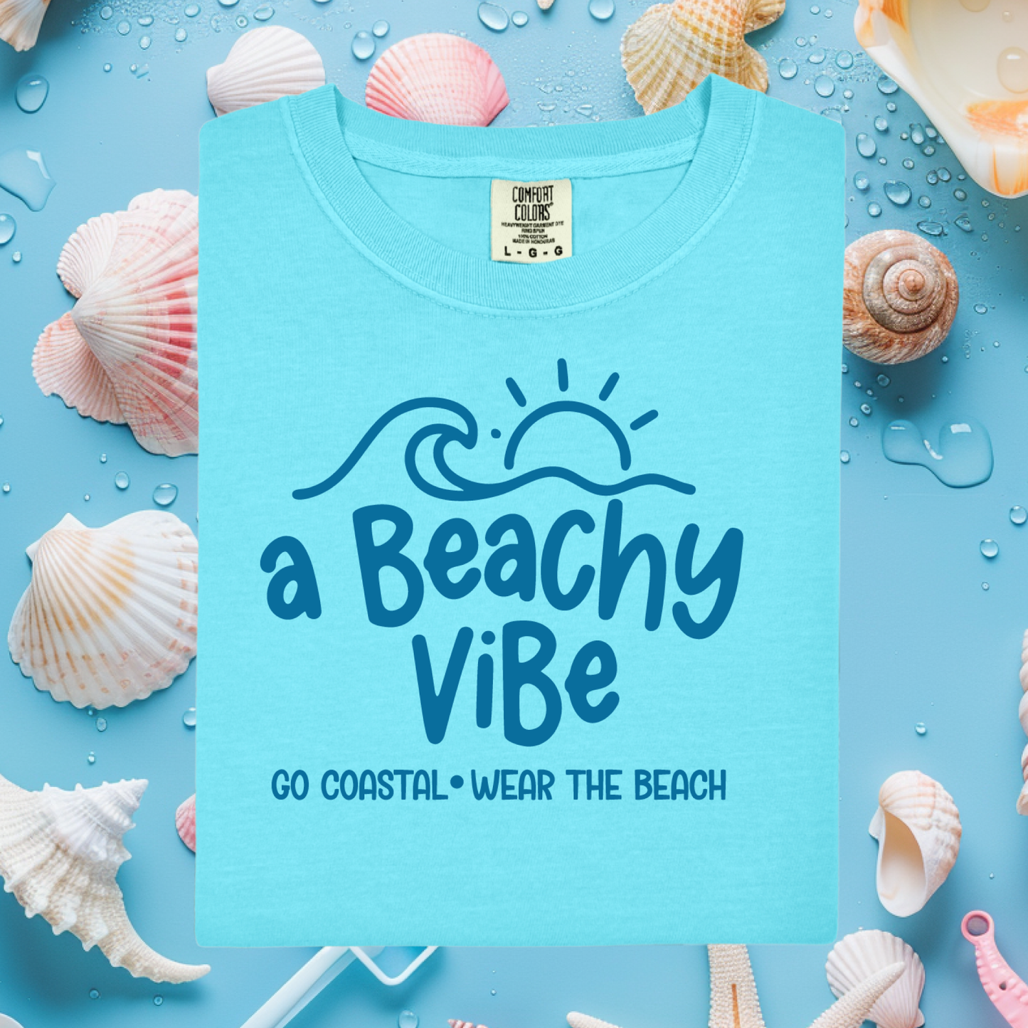 Blue t-shirt with 'a Beachy Vibe' text surrounded by seashells on a blue background